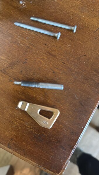 Pièces métalliques démontées pour réparation de serrure : broches, tige filetée et plaque de came sur table en bois