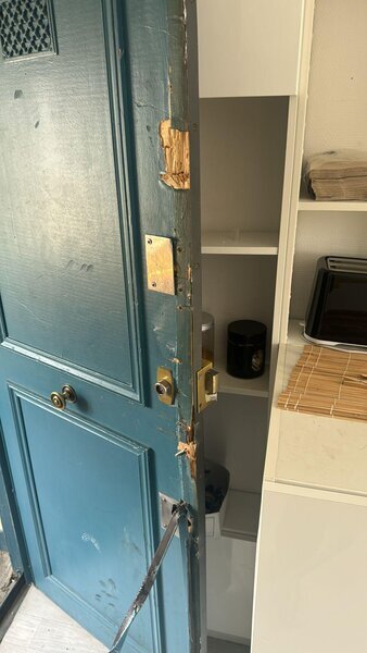 porte d'entrée bleue endommagée après effraction, bois éclaté au niveau de la serrure, renfort métallique installé